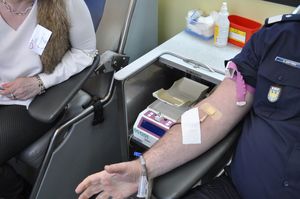 Na zdjęciu widoczna ręka osoby oddającej krew oraz sylwetka kobiety z obsługi ambulansu do pobierania krwi.