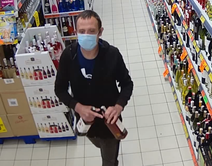 zdjęcie kolorowe: młody mężczyzna w maseczce na twarzy zarejestrowany przez kamery monitoringu sklepowego