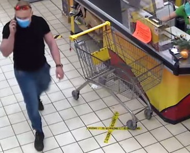 zdjęcie kolorowe: zapis z monitoringu sklepowego przedstawiający mężczyznę podejrzewanego  kradzież alkoholu, ubrany w niebieskie długie jeansy, czarna koszulkę typu polo z krótkim rękawem, niebieską maseczkę ochronną założoną na usta i okulary przeciwsłoneczne czarne z błyszczącymi pomarańczowymi szybkami, które założone są na głowie    