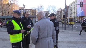 Policjanci wraz z księdzem wręczają pieszym elementy odblasko