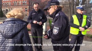 Policjanci wraz z księdzem wręczają pieszym elementy odblasko