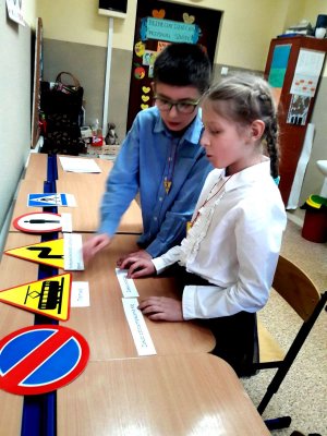 dzieci rozwiązują zadania konkursowe przed nimi stolik a na nim znaki drogowe