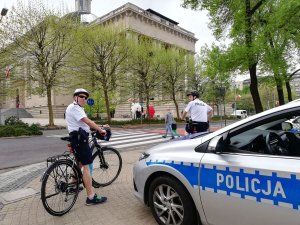 policjanci jadą na rowerach przed nimi stoi Katedra w Katowicach za nimi stoi radiowóz policyjny