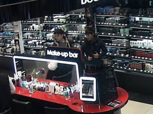 Na zdjęciu widać dwóch sprawców kradzieży perfum jak stoją za regałem w sklepie