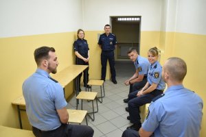 Na zdjęciu widać jak polscy policjanci stoją w pomieszczeniu dla osób zatrzymanych i opowiadają o pracy niemieckim kolegom którzy siedzą