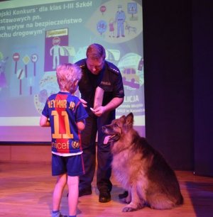 Na zdjęciu widać policjanta z psem którzy wręczają dziecku naklejkę