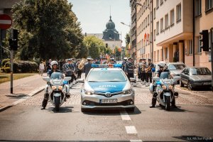 na zdjęciu widać radiowóz policyjny oraz motocykle a na nich policjantów ruchu drogowego z tyłu stoi orkiestra policyjna