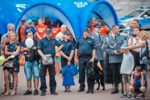 na zdjęciu widać trzech stojących policjantów i psa służbowego obok przemieszczają się odwiedzający festyn oraz inni policjanci