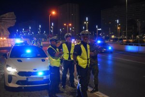 Na zdjęciu widać trzech policjantów ruchu drogowego oraz żołnierza jak stoją obok nieoznakowanego radiowozu na rondzie, radiowóz ma włączone sygnały świetlne
