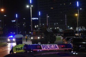 Na zdjęciu widać policjantów ruchu drogowego, obok radiowozu przednimi jedzie czołg w tle stoi też radiowóz