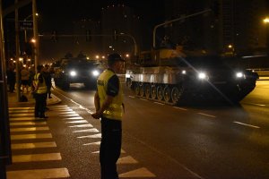 Na zdjęciu widać policjantkę i policjant jak  zabezpieczają skrzyżowanie przed nimi jedzie kolumna czołgów w tel widać osiedle gwiazdy