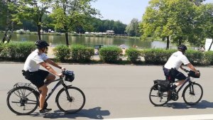 Na zdjęciu widać dwóch policjantów jadących na rowerach za nimi widać krzaki, plażę i staw