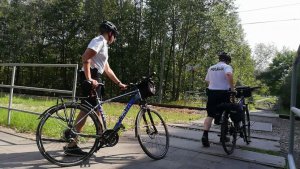 Na zdjęciu widać dwóch policjantów prowadzących rowery przez przejazd kolejowy