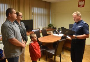 Na zdjęciu widać małżeństwo z dzieckiem oraz Zastępce Komendanta Miejskiego Policji w Katowicach w swoim gabinecie jak wręcza list gratulacyjny