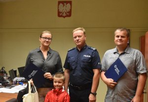 Na zdjęciu widać małżeństwo z dzieckiem oraz Zastępce Komendanta Miejskiego Policji w Katowicach w swoim gabinecie jak stoją. Małżeństwo trzyma listy gratulacyjne
