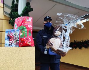 Zdjęcie kolorowe,umundurowany policjant niosący prezent świąteczny.