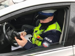 zdjęcie kolorowe: policjant drogówki w radiowozie sporządzający dokumentacje z kontroli drogowej