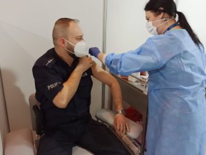 zdjęcie kolorowe:
 umundurowany policjant podczas podawania szczepionki przez pielęgniarkę