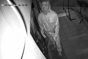 zdjęcie czarno-białe: ujęcie z kamery monitoringu zamaskowany mężczyzna stojący przed drzwiami sklepu