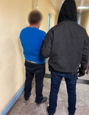 zdjęcie kolorowe: korytarz na którym jest mężczyzna trzymany za ramię przez policjanta wydziału kryminalnego