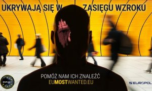 zdjęcie kolorowe: na tle żółtej ściany zamazany obraz mężczyzny, za plecami którego przechodzą ludzie oraz napis o treści: ukrywają się w zasięgu wzroku. Pomóż nam ich znaleźć. EUMOSTWANTED.EU