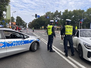 zdjęcie kolorowe: policjanci drogówki na skrzyżowaniu zabezpieczający trasę biegu