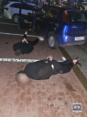 Na zdjęciu leżący na chodniku i skuci kajdankami zatrzymani mężczyźni.