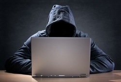 zdjęcie kolorowe: mężczyzna z kapturem na głowie siedzi przy biurku przed laptopem