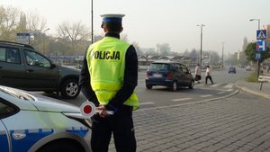 zdjęcie kolorowe: policjant drogówki nadzorujący ruch samochodów w rejonie oznakowanego przejścia dla pieszych